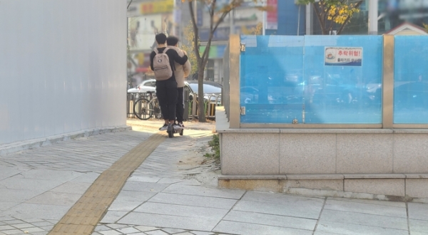 ▲ 27일 수원시청역 인근에서 헬맷도 착용하지 않은 남성 2명이 전동 킥보드를 함께 타고 이동하고 있다. (사진=신연경 기자)