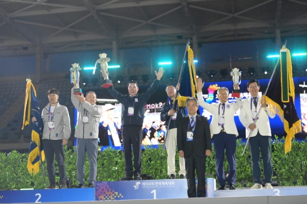 ▲ 19일 전남 목포시 목포종합경기장에서 열린 제104회 전국체육대회 폐회식에서 종합우승 2연패를 차지한 경기도선수단을 대표해 이원성 경기도체육회장(왼쪽 세번째)과 김택수 총감독(경기도체육회 사무처장)이 종합우승컵과 우승기를 들고 기념사진을 찍고 있다. (사진=유창현 기자)