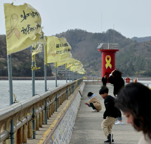 세월호 참사 11주기를 앞둔 13일 오후 전남 진도군 팽목항 방파제에 설치된 빛바랜 깃발이 바람에 날리고 있고, 참배객들이 기록물을 살펴보고 있다. /전남 팽목항 =김철빈 기자